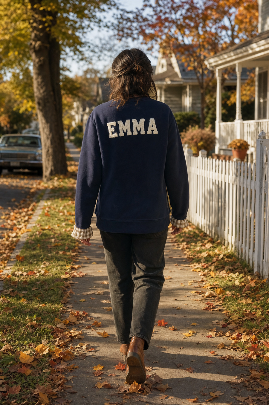 A woman walking away down an autumn street with EMMA embroidered across the back of her sweatshirt