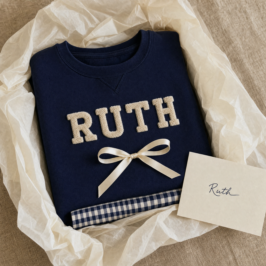 A folded navy RUTH sweatshirt in cream tissue with a ribbon and a handwritten card