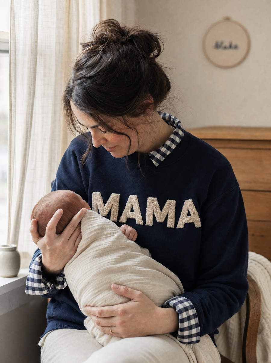 A new mother in a MAMA mockneck holding her baby by a nursery window
