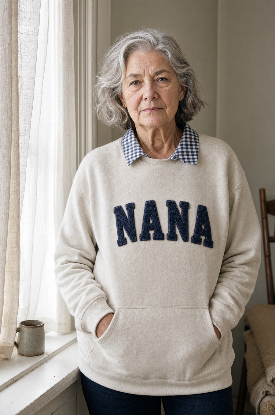 A woman in her seventies by a window in an oatmeal sweatshirt with NANA in navy chenille